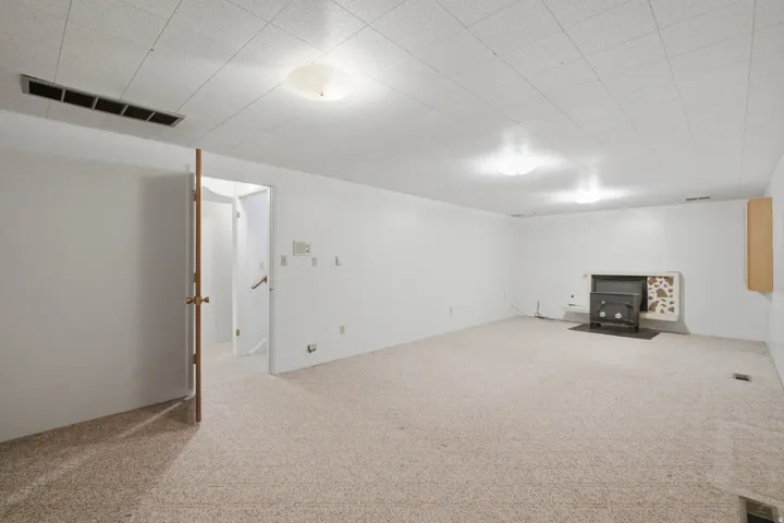 Spacious room featuring light-colored carpet flooring, recessed ceiling tiles, and flush-mount lighting fixtures