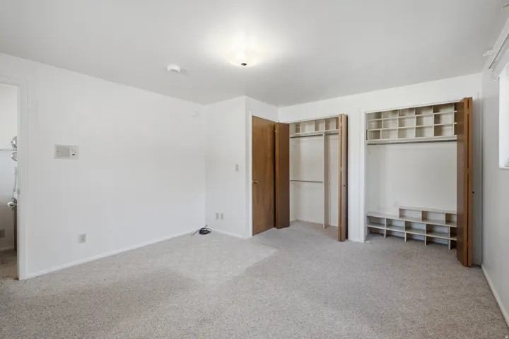 Carpeted room featuring two bifold door closets with built-in shelving and hanging rods, white walls, and a flush-mount ceiling light fixture