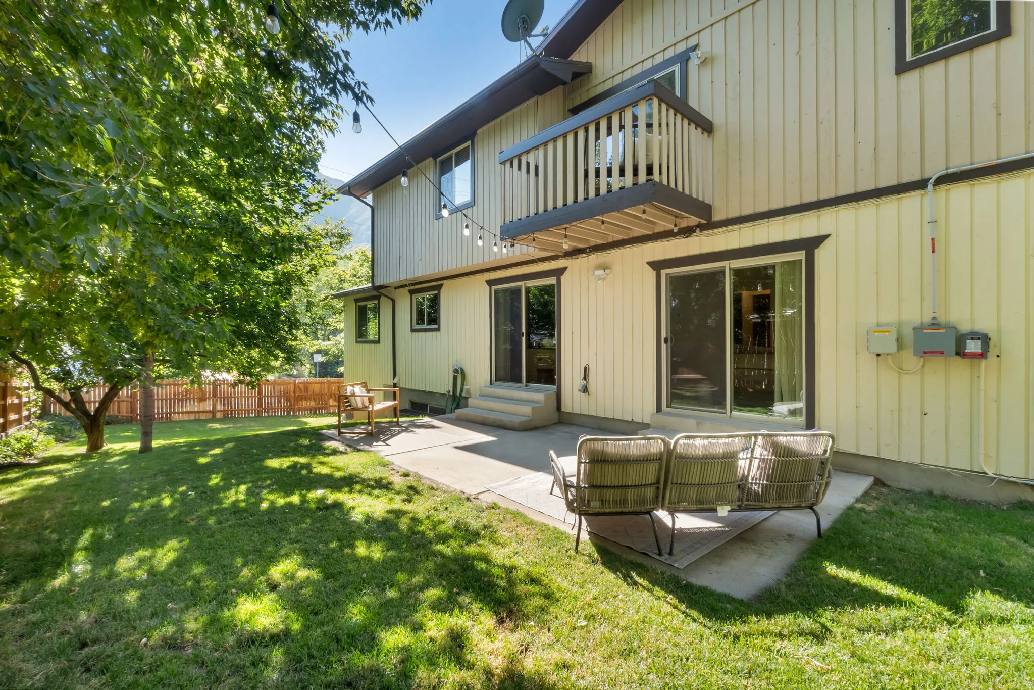 Rear exterior featuring two sliding glass doors, a concrete patio, and a second-story balcony