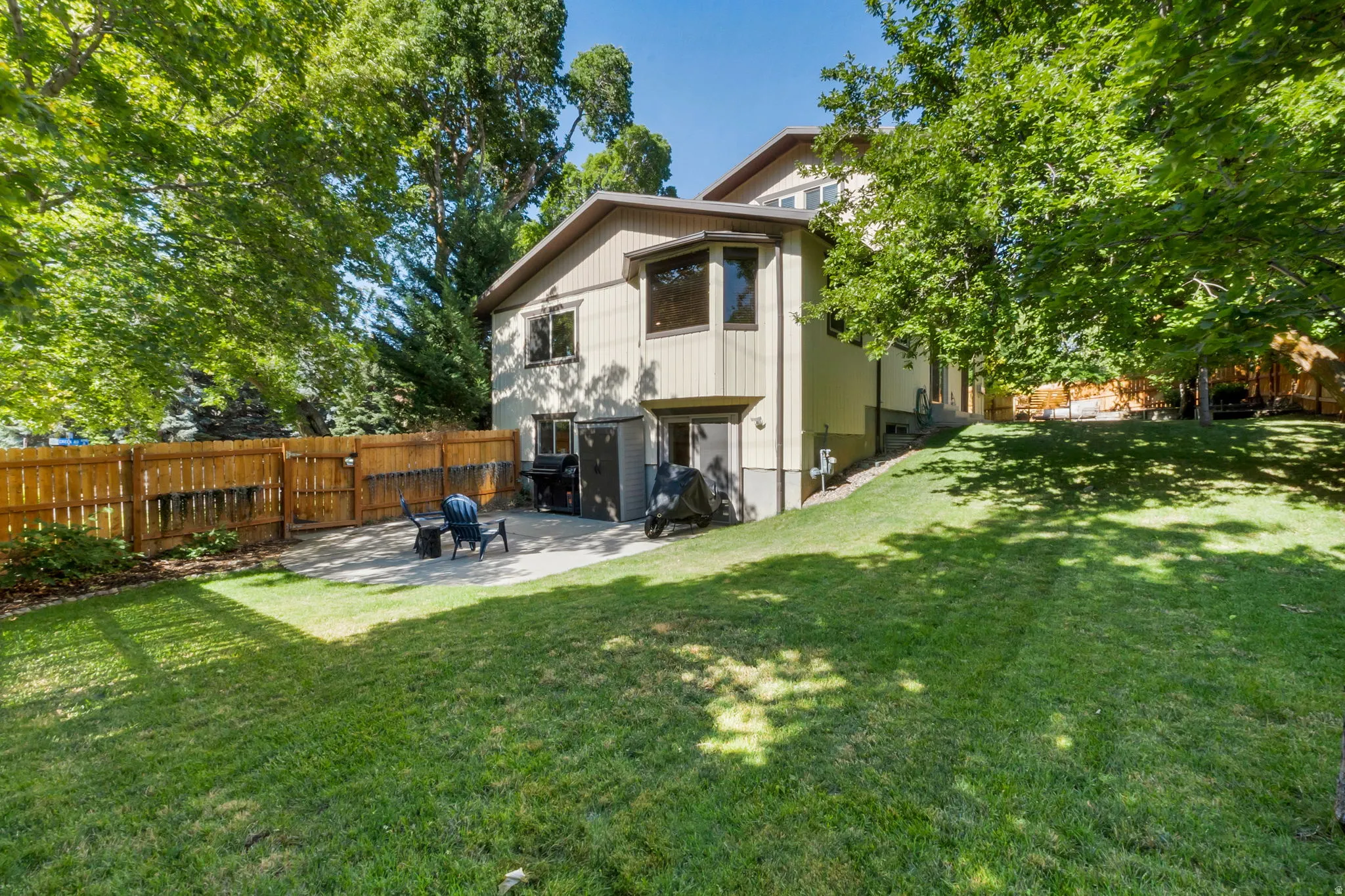 Expansive backyard featuring a lush lawn, mature trees, a privacy fence, and a concrete patio
