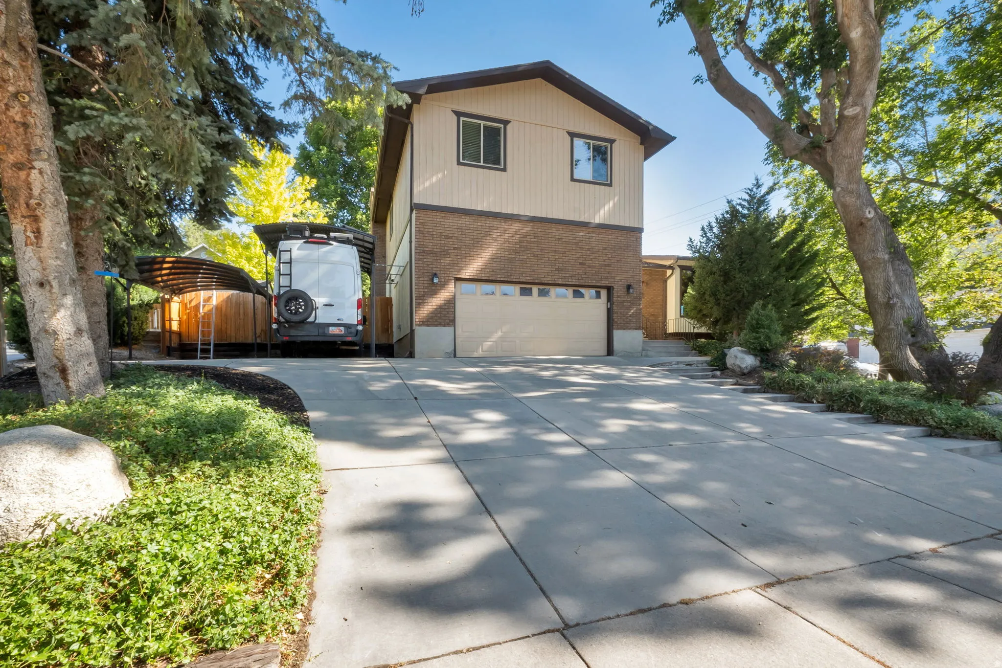 Multistory exterior with a two-car garage, brick and siding facade, mature trees, and a spacious concrete driveway