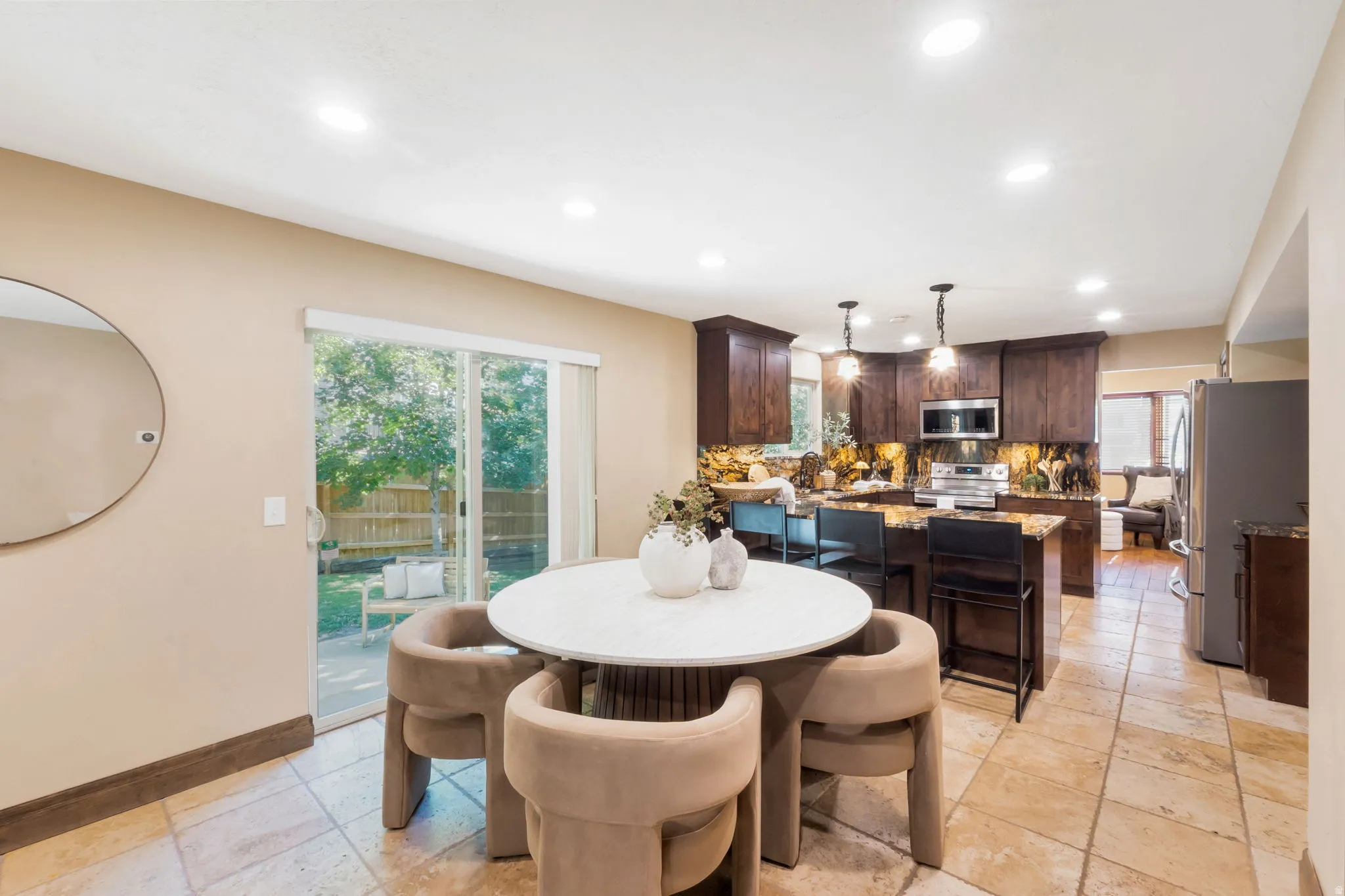 Open-concept kitchen and dining area featuring tile flooring, dark wood cabinetry, a granite island with seating, and stainless steel appliances