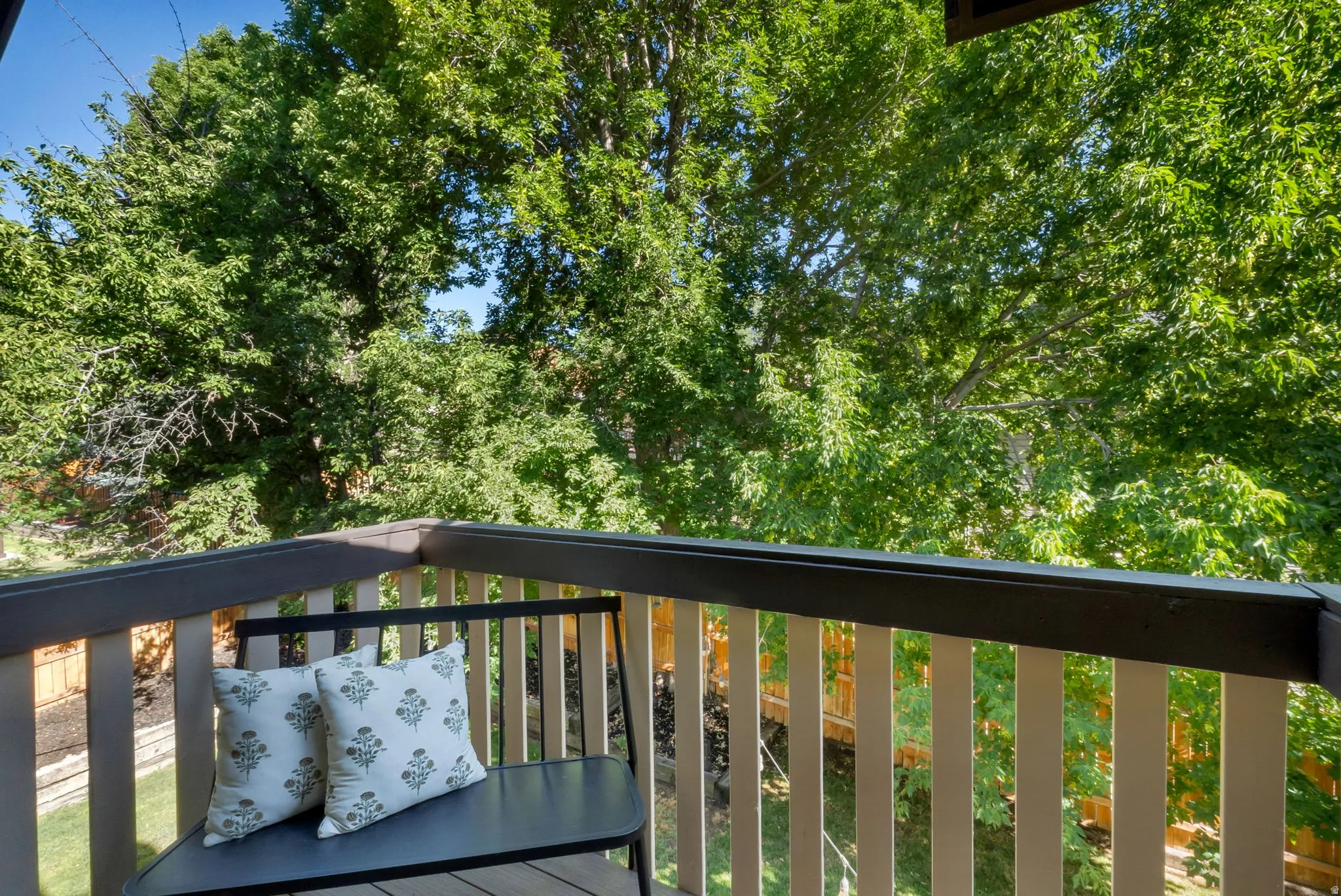 Private balcony with dark wood railing and slatted balusters overlooking mature trees and a fenced yard