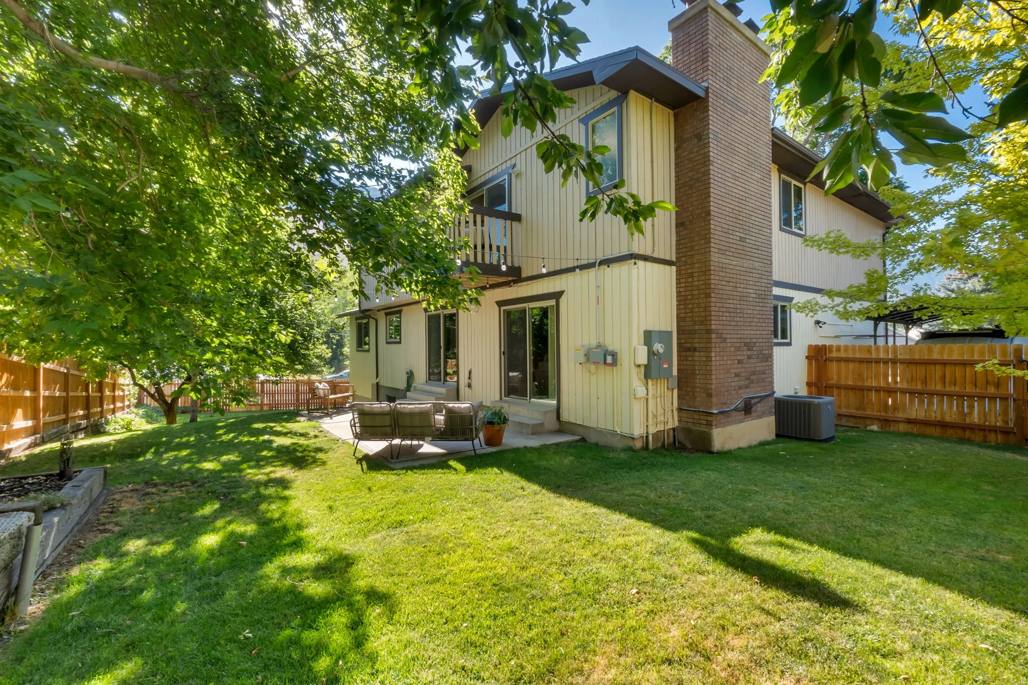 Rear exterior featuring a brick chimney, a privacy fence, a second-story balcony, and a ground-level patio