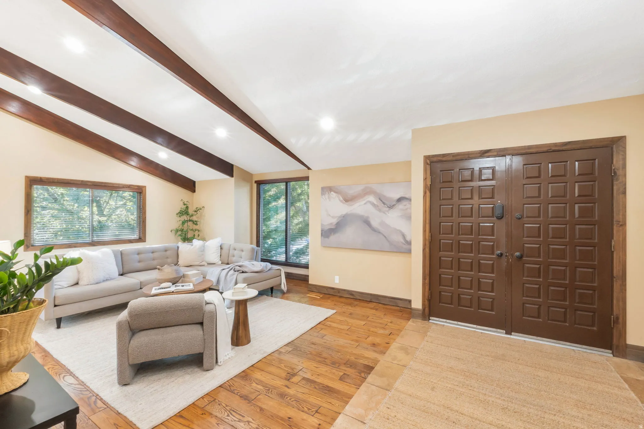 Entryway featuring double panel doors with a natural wood finish, leading to a living area with vaulted ceilings, exposed wood beams, wood-finish flooring, and expansive windows