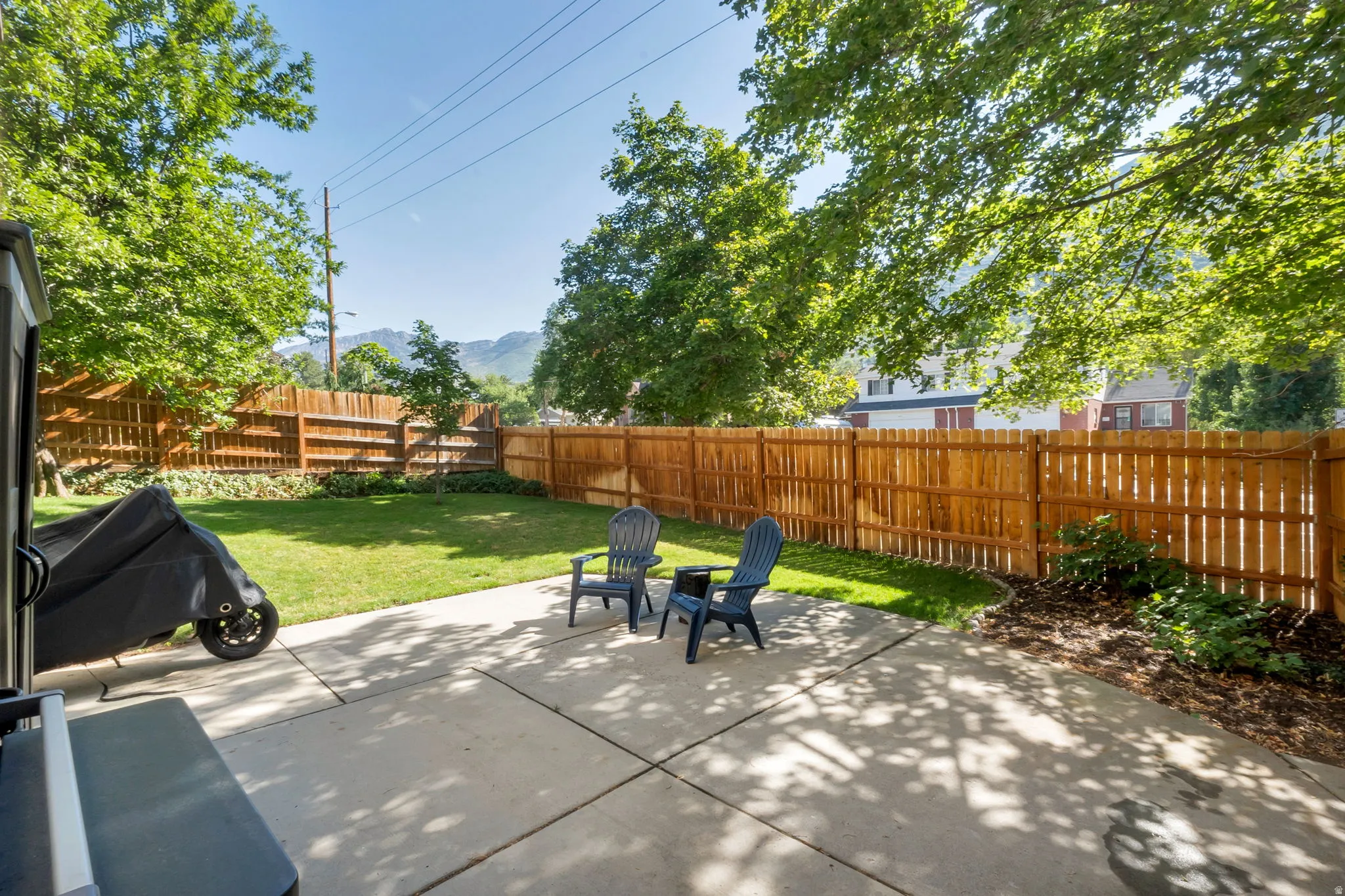Expansive backyard featuring a concrete patio, a manicured lawn, and mature trees