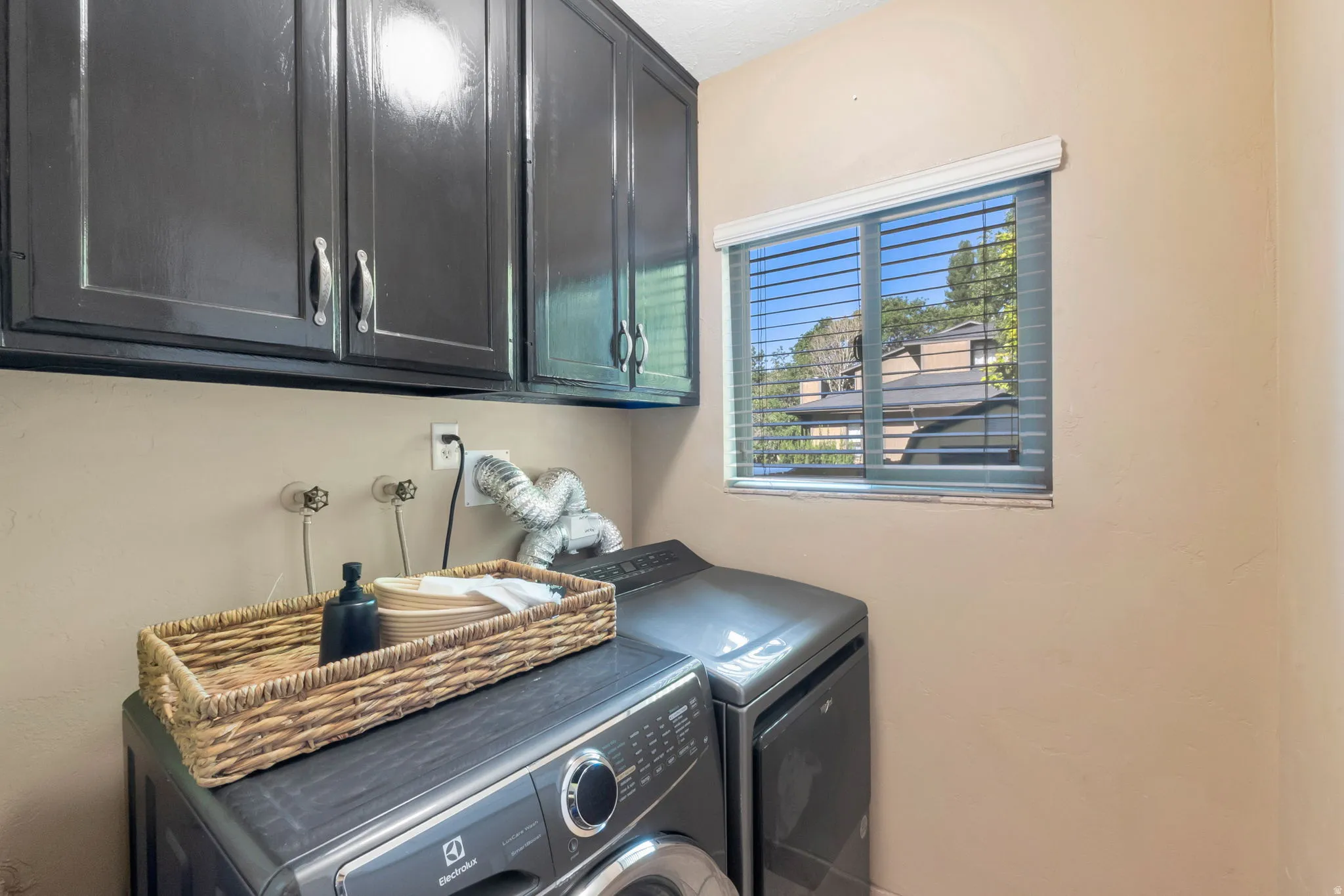 Laundry area featuring dark cabinetry with brushed nickel hardware, a window with horizontal blinds, and beige walls