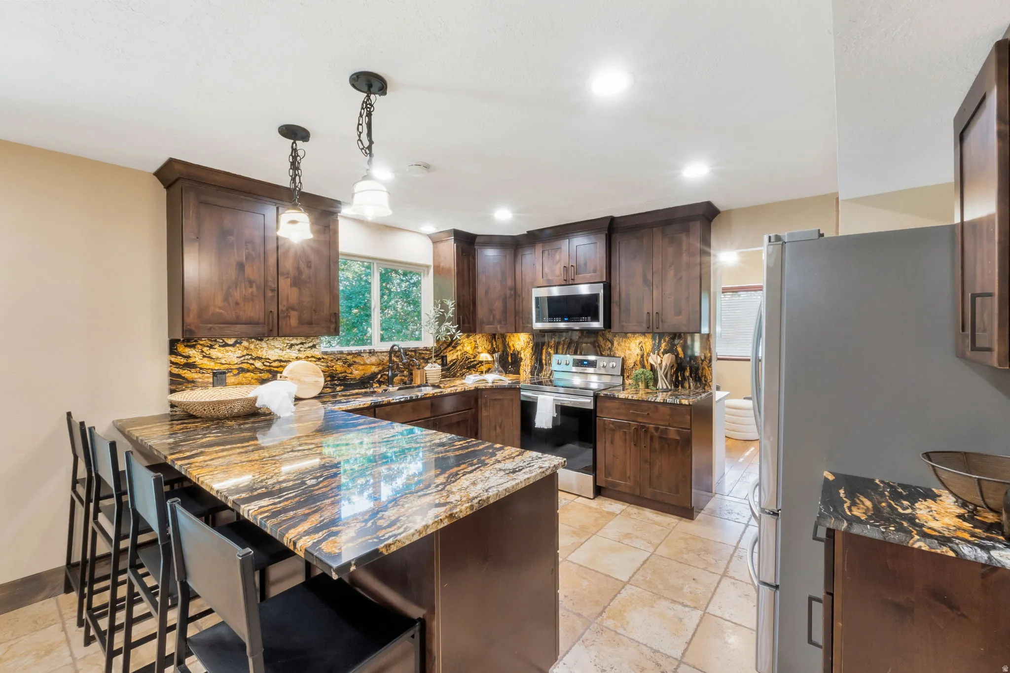 Kitchen featuring dark wood cabinetry, patterned stone countertops and backsplash, stainless steel appliances, recessed lighting, and tile flooring