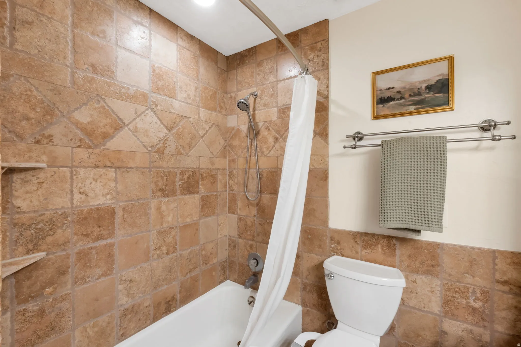 Bathtub with a multi-function shower head, surrounded by earth-toned tile with a decorative accent band