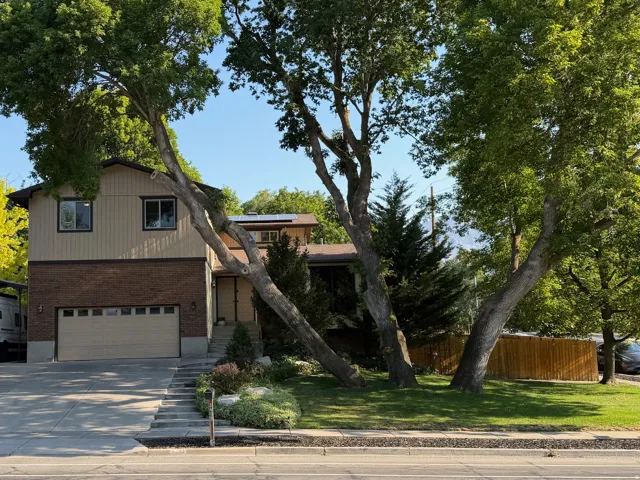 Split-level residence featuring a two-car garage, brick and vertical siding exterior, and mature trees