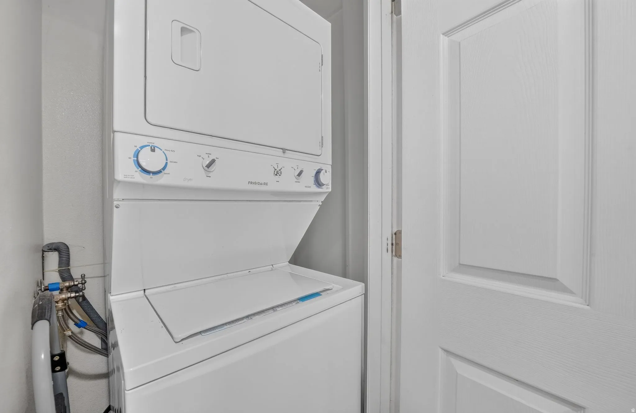 Dedicated laundry room featuring a stackable washer and dryer unit with intuitive controls, white finish cabinetry, tile flooring, and convenient wall-mounted storage solutions for household essentials