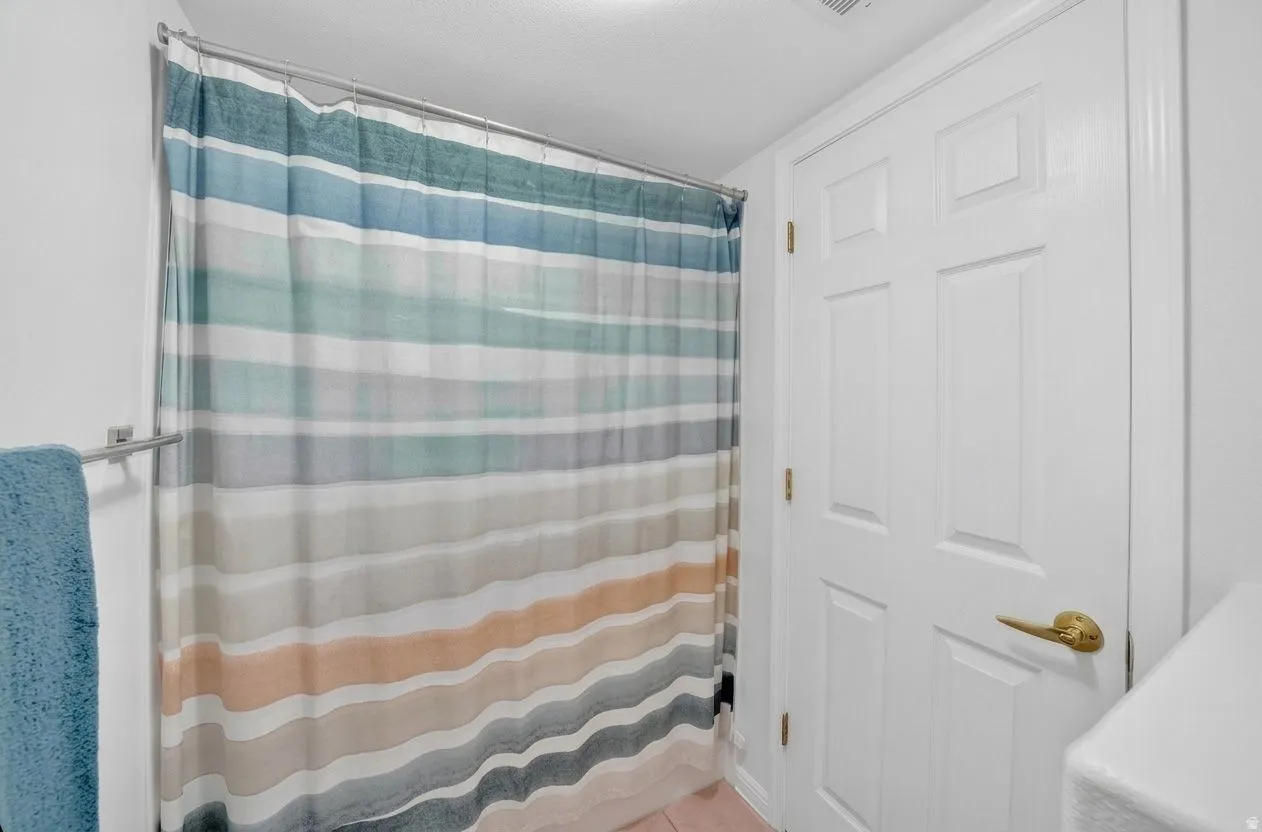 Clean and bright bathroom featuring a white six-panel door with brass hardware, ceramic tile flooring, and a striped shower curtain in soft teal, beige, and charcoal tones