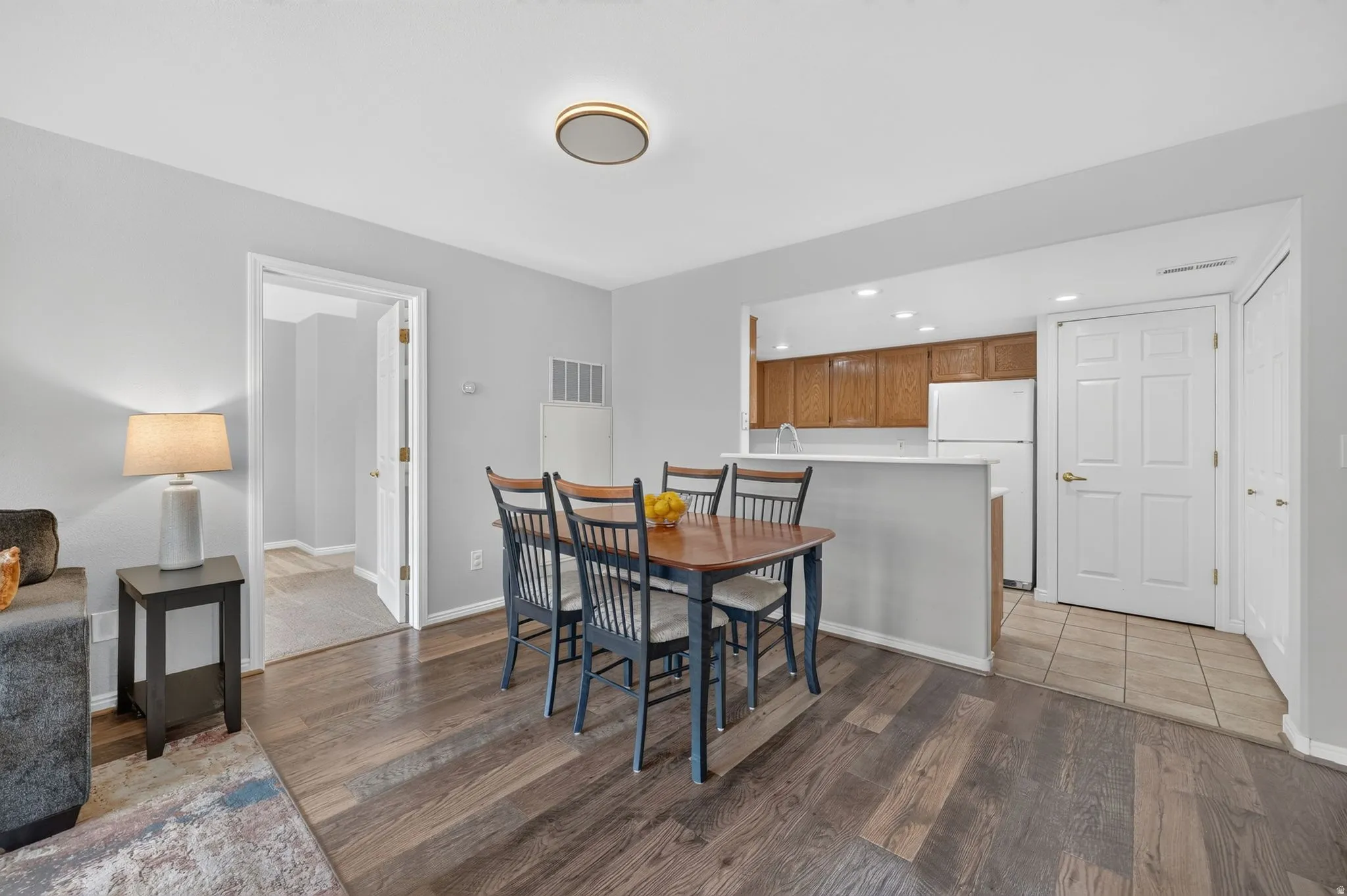 Open-concept living and dining area featuring wood-finish flooring, a dining table with seating for four, and direct access to the kitchen with white cabinetry and wood-tone upper storage