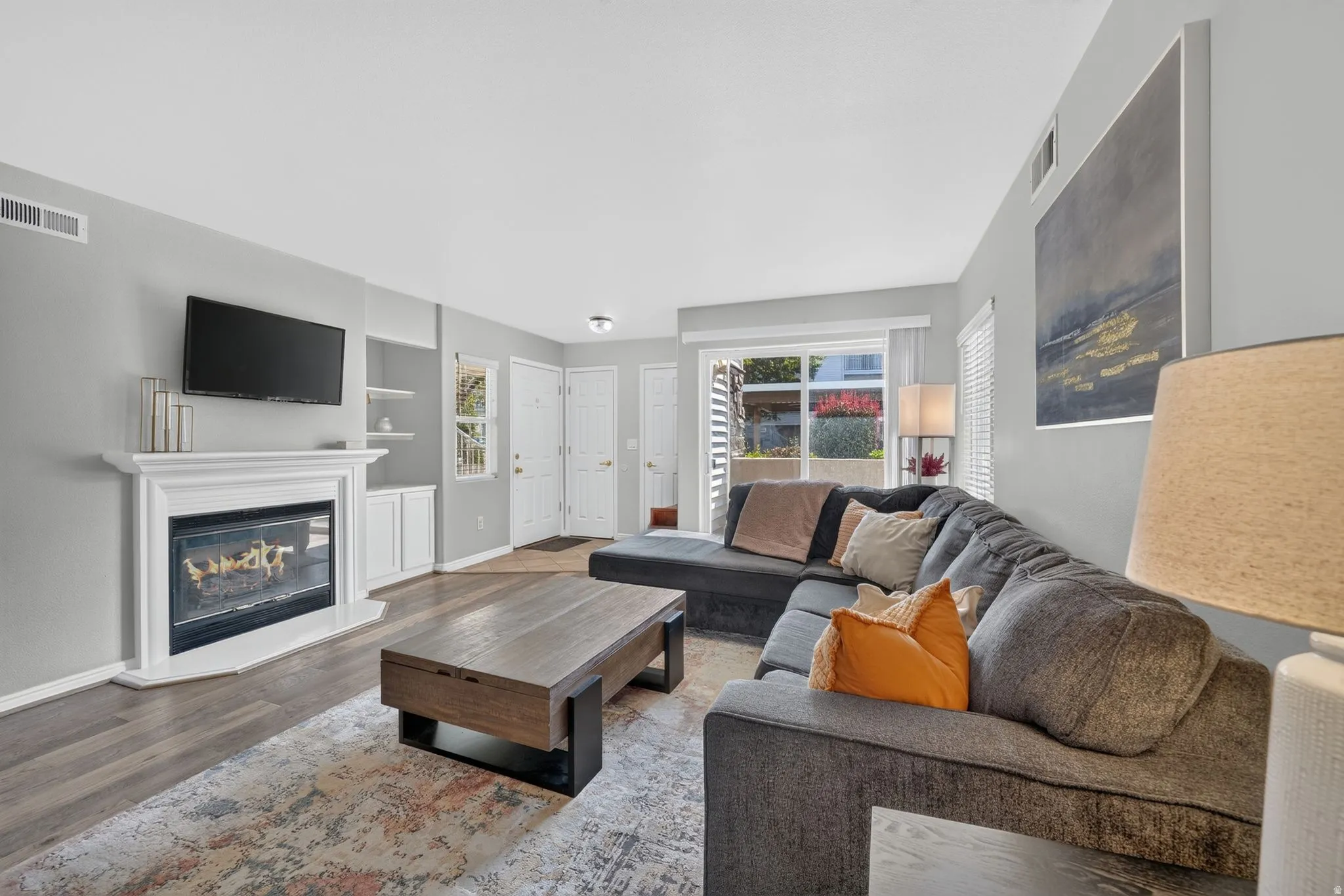 Living area featuring wood-finish flooring, a white mantel fireplace, and built-in shelving