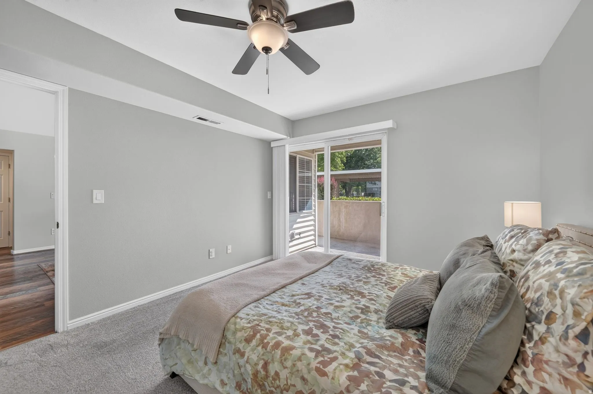 Spacious bedroom featuring neutral gray walls, plush carpeting, and abundant natural light from sliding glass doors opening to an outdoor patio
