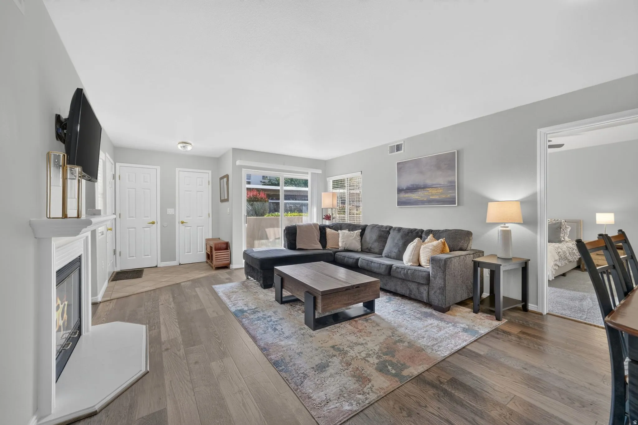 Bright and open living room featuring a wood-finish plank floor, gas fireplace with white surround, and ample natural light from multiple windows