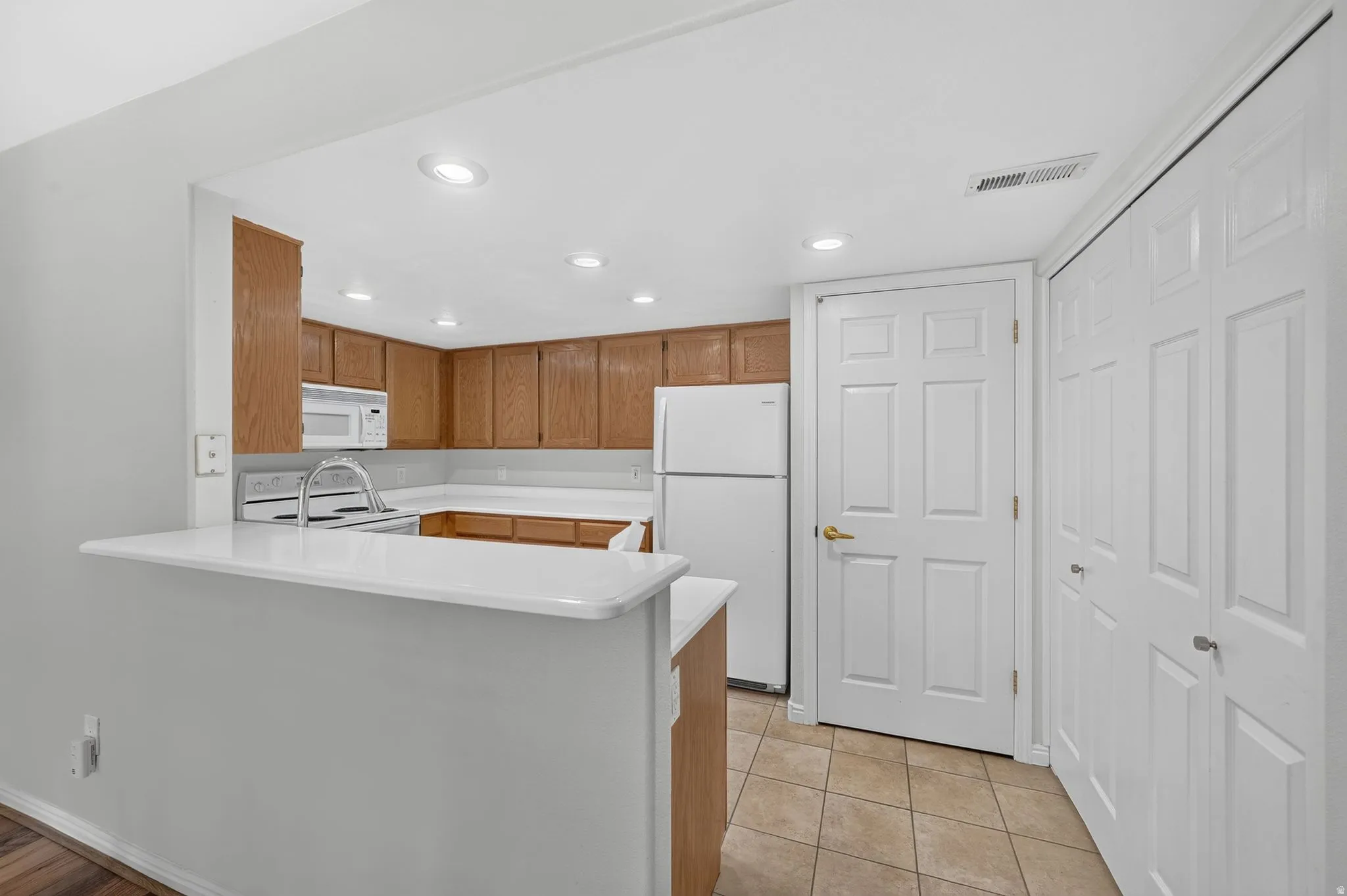 Open kitchen featuring warm wood-finish cabinetry, white appliances, and a white quartz countertop breakfast bar