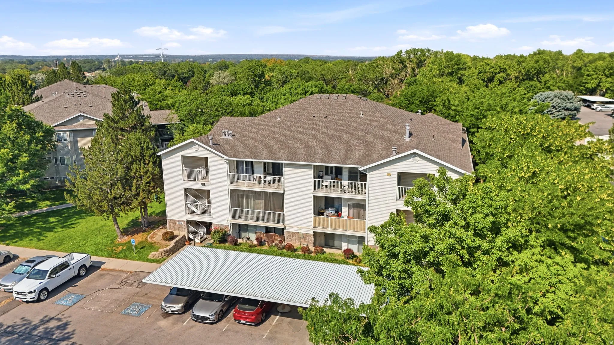 Multi-level residential building featuring a clean white exterior with brown dimensional shingle roofing, multiple balconies with metal railings, and large window openings throughout