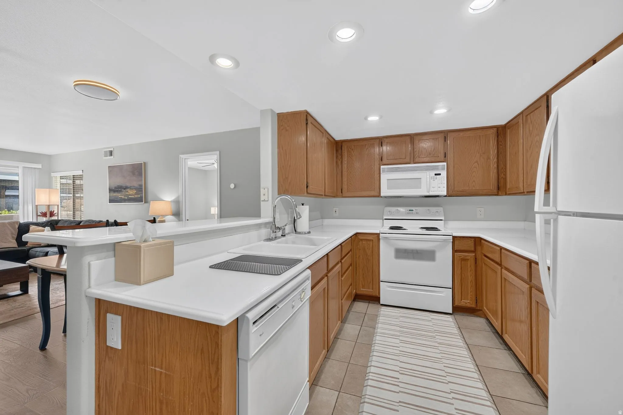Spacious kitchen featuring warm wood cabinetry, white appliances, and a center island with cooktop