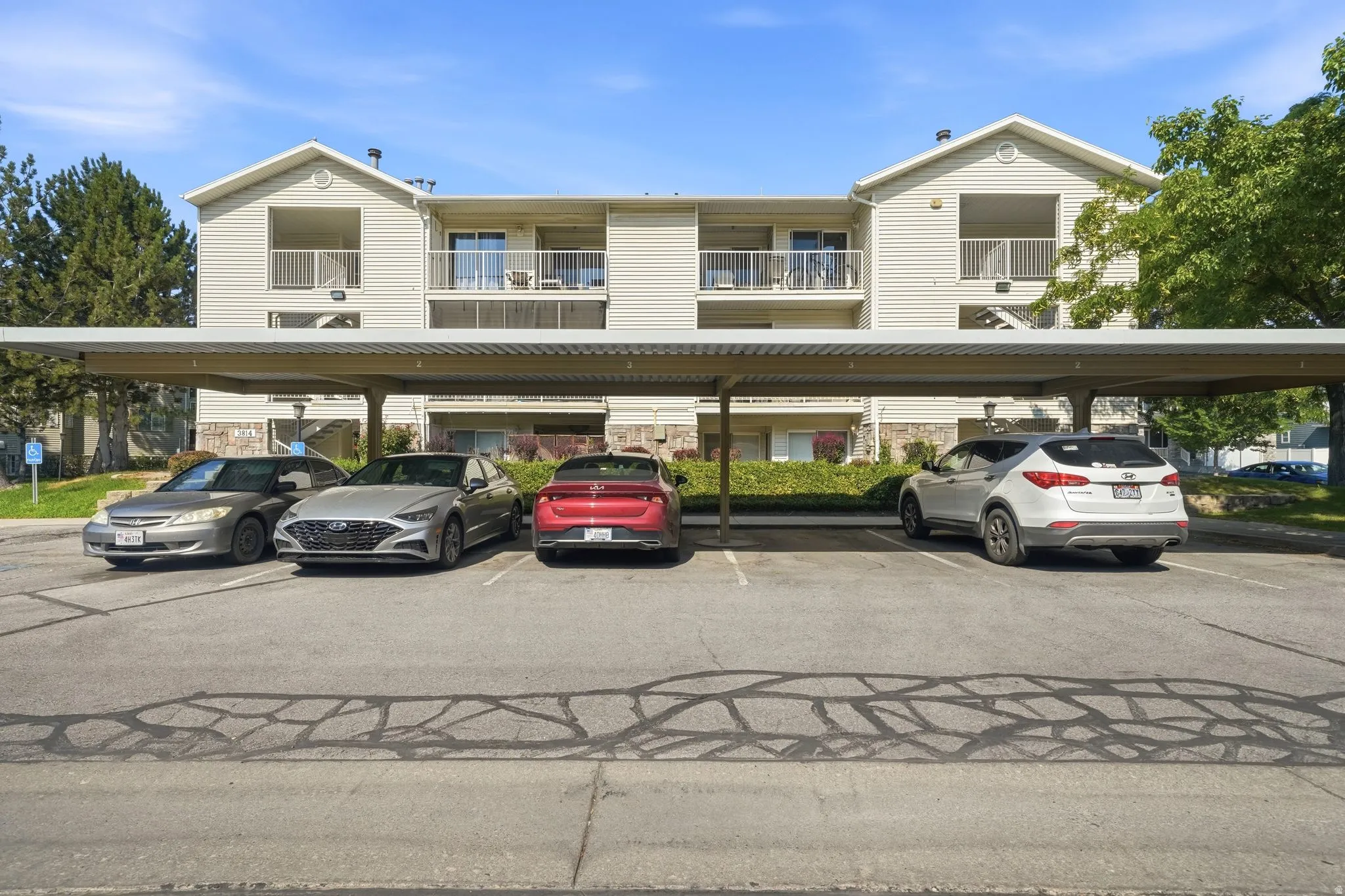Modern multi-unit residential building featuring clean cream-colored siding, pitched rooflines with gabled details, and expansive covered parking structure