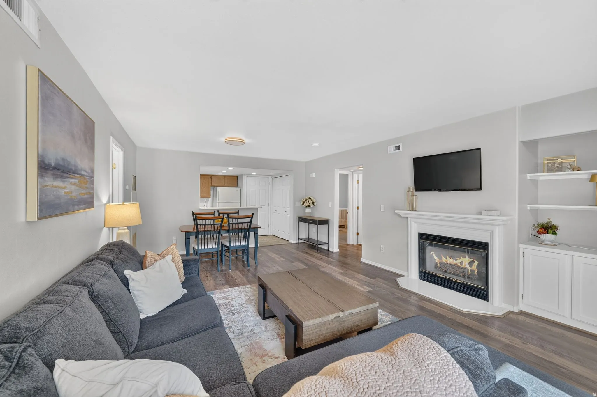 Living area featuring wood-finish flooring, a white mantel fireplace, and built-in shelving with cabinetry