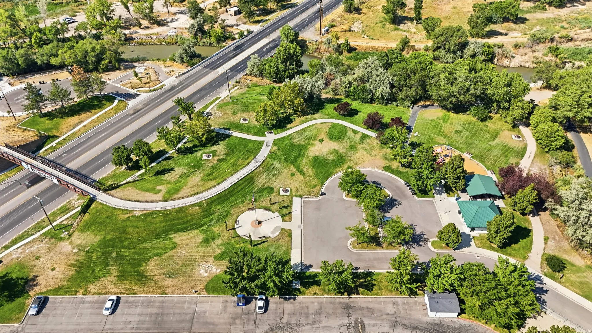 Expansive park area featuring paved paths, mature trees, green spaces, and a covered structure with a green roof