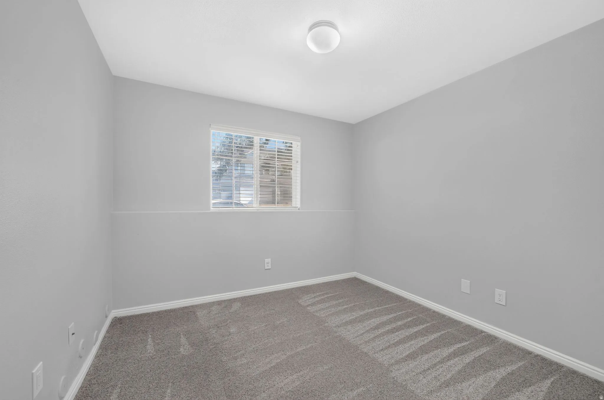 Bright, neutral bedroom featuring neutral wall finishes, recessed ceiling lighting, a large window with plantation shutters providing natural light, and carpeted flooring in mixed tones