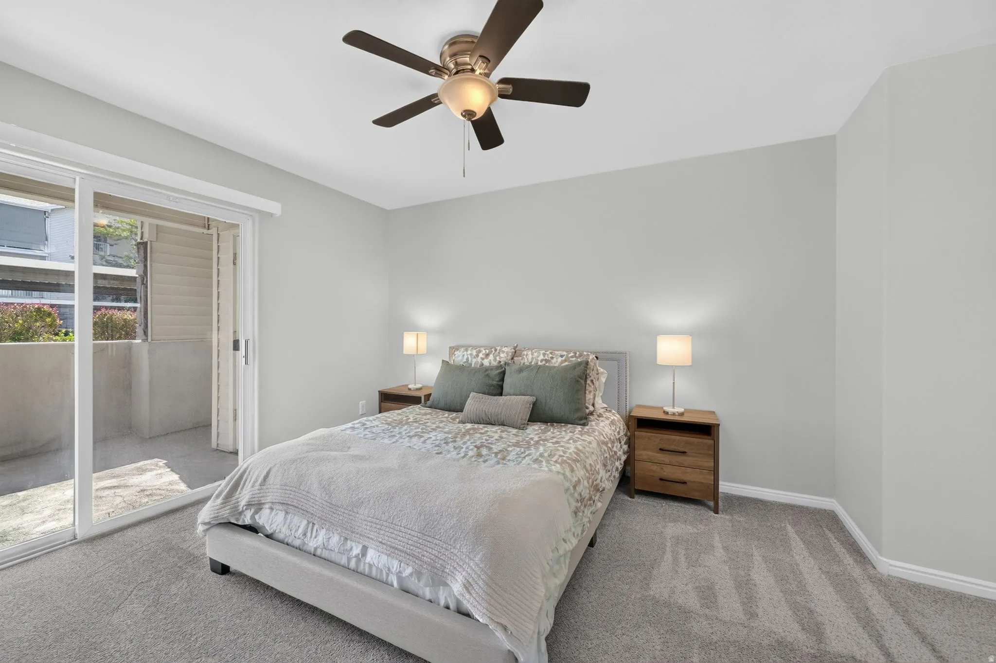 Spacious primary bedroom featuring soft neutral walls, carpeted flooring, and abundant natural light from glass sliding doors opening to an outdoor patio