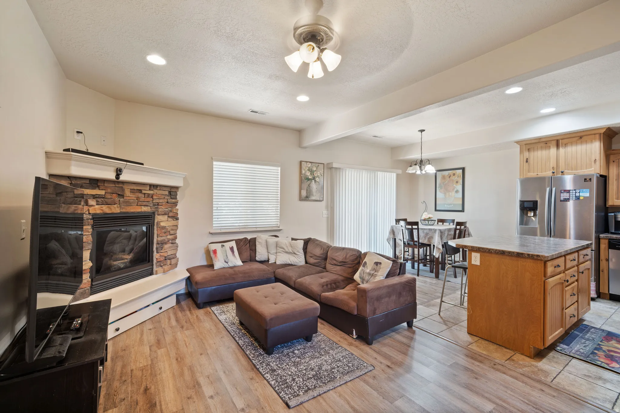 Open-concept living area featuring wood-finish flooring and a stone-faced fireplace with a white mantel
