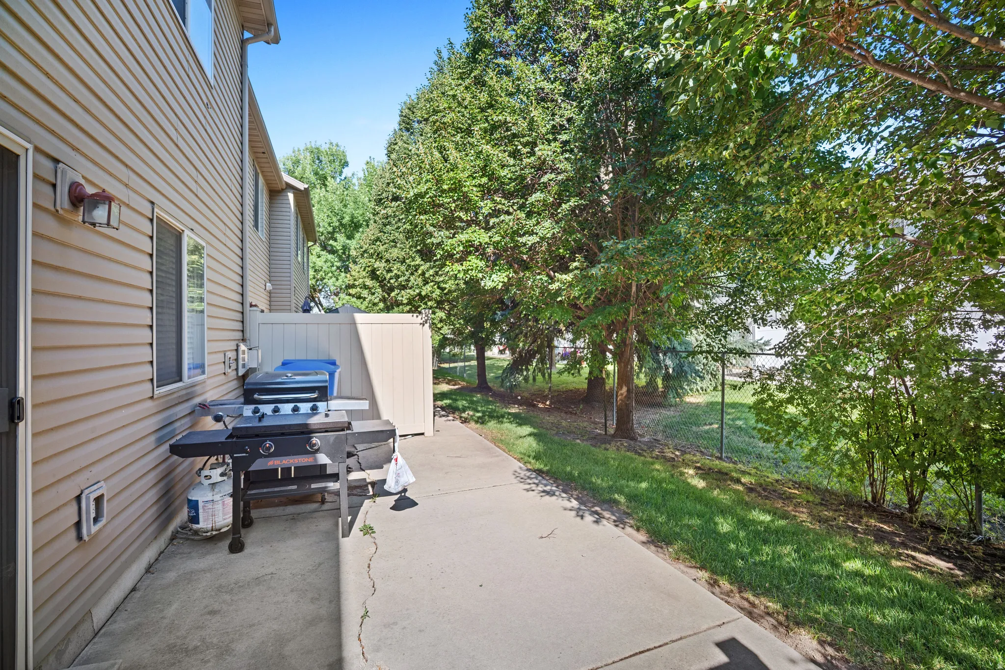 Concrete patio area bordered by mature trees and a chain-link fence