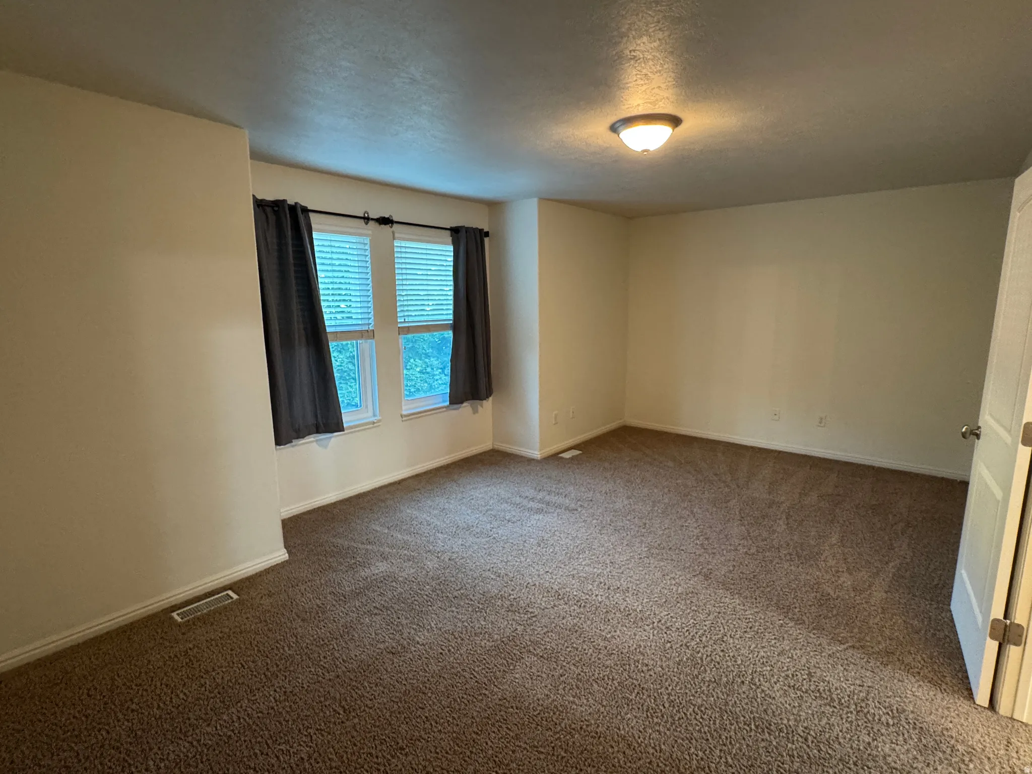 Spacious room featuring neutral carpeting, light-toned wall paint, and two windows with blinds