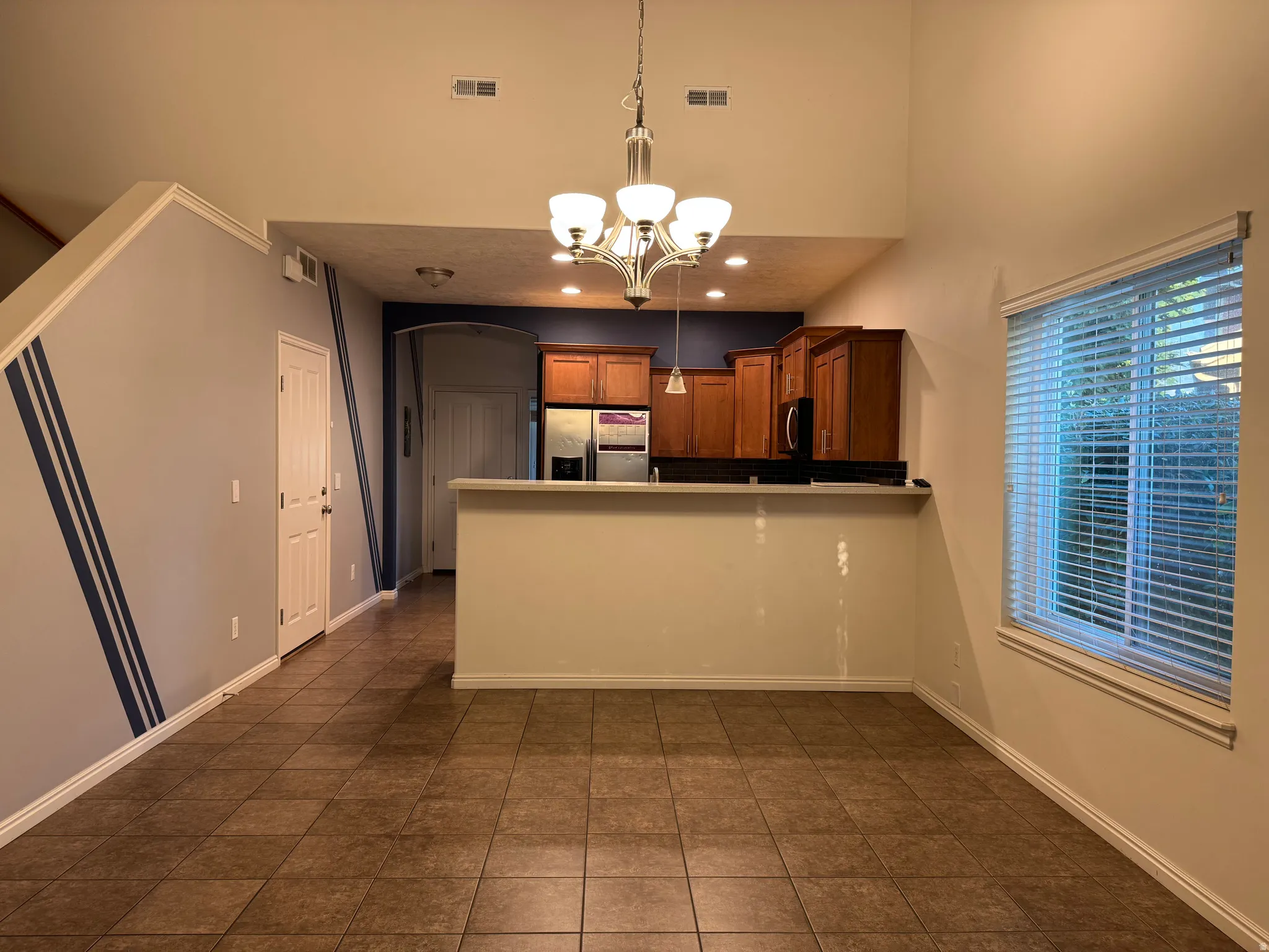 Open dining and kitchen area featuring a wood-finish island with breakfast bar seating, wood cabinetry with stainless steel appliances, tile flooring throughout, recessed lighting, and a pendant light fixture