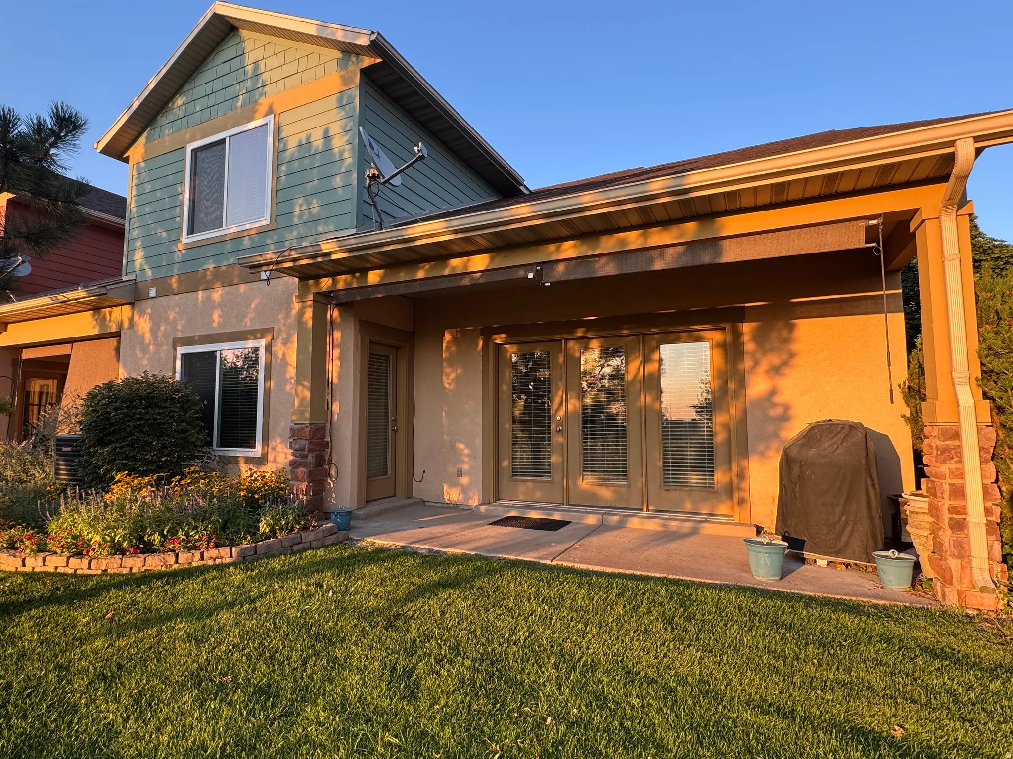 Charming two-story residence featuring a covered patio with wooden beam construction, expansive manicured lawn, and mixed siding exterior with upper-level gable detailing