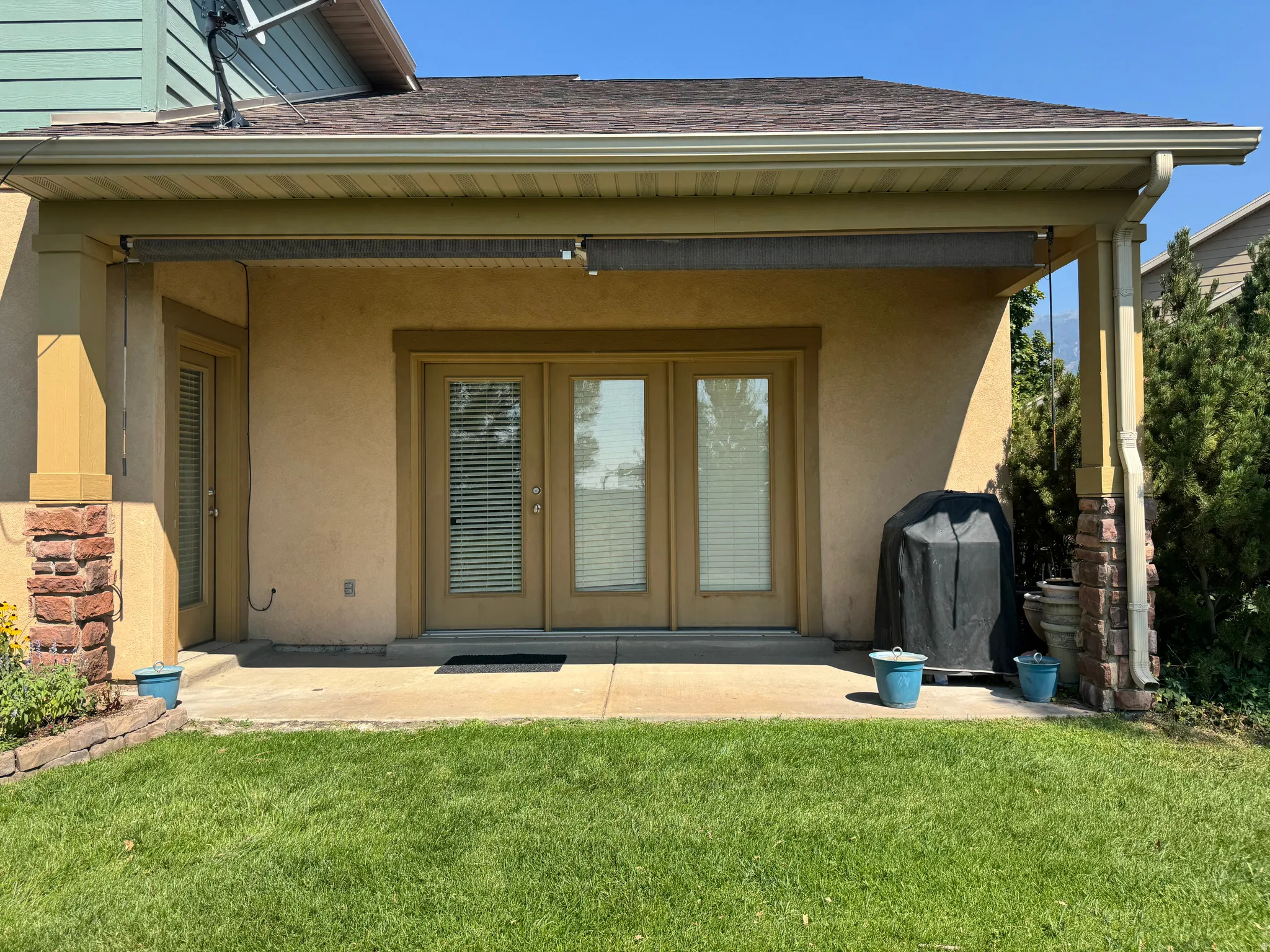 Ground-level patio with stucco exterior and French doors, featuring a retractable awning and brick-clad columns