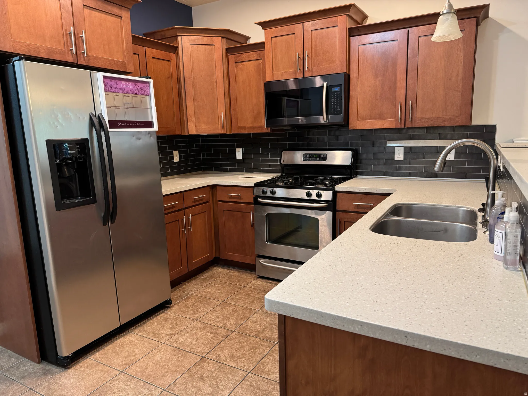 Kitchen featuring wood cabinetry, light-toned countertops, stainless steel appliances, and a dark subway tile backsplash