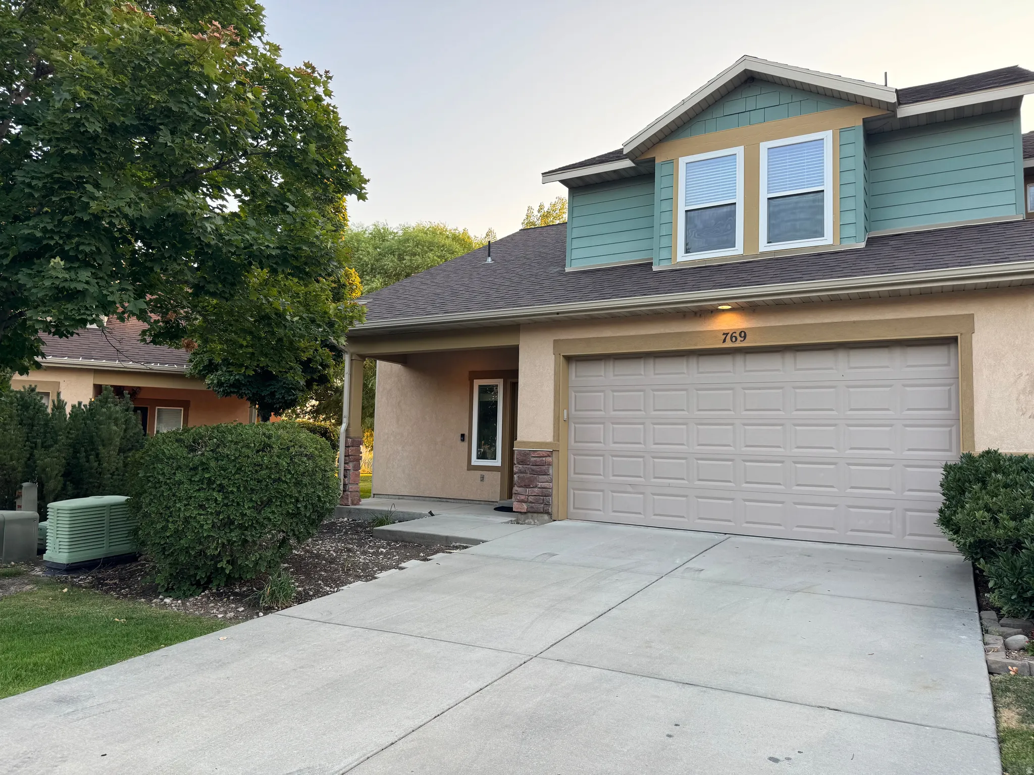 Stucco exterior featuring a two-car garage, concrete driveway, and a covered entry with stone accents