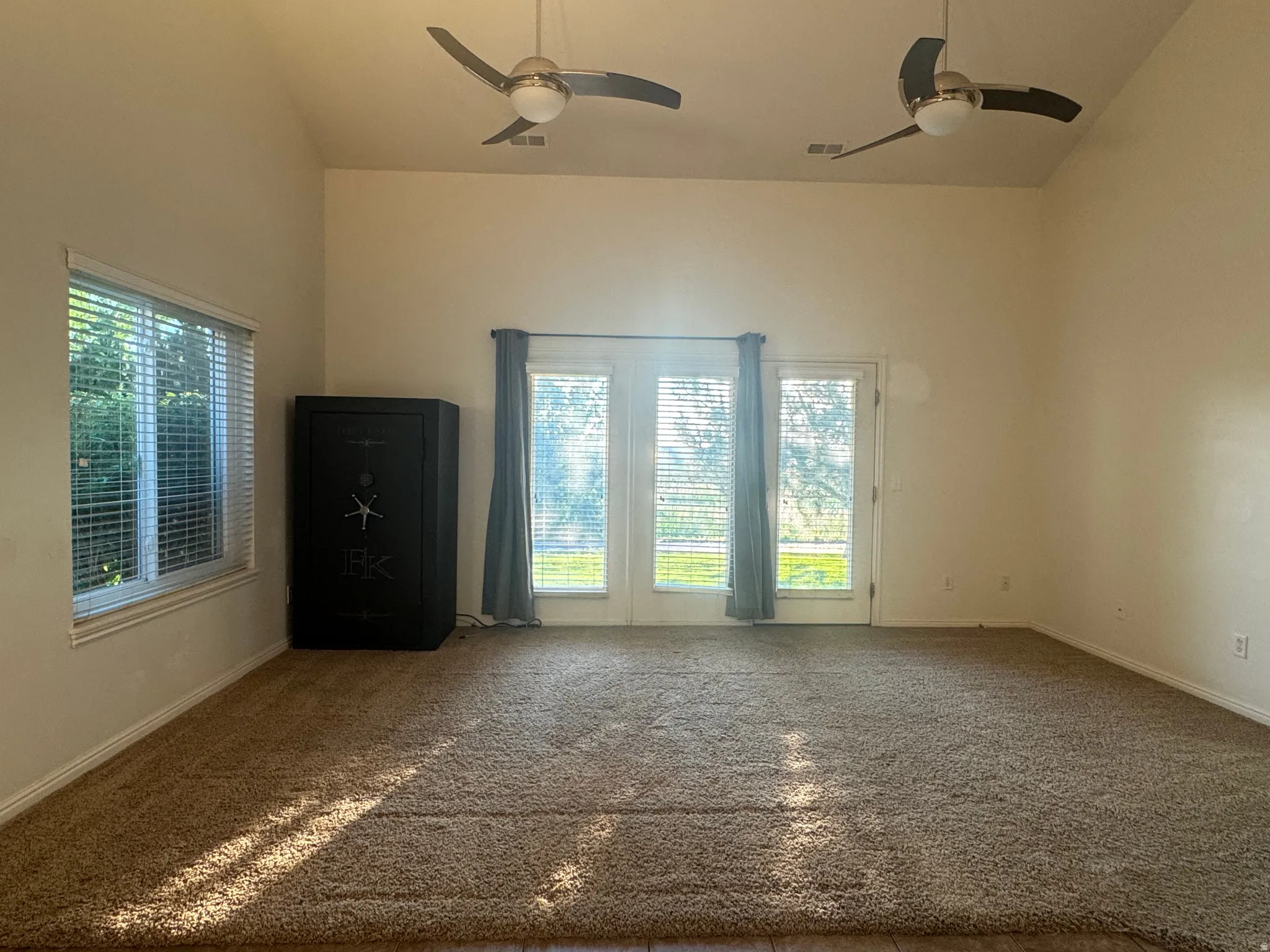 Spacious open room with dual ceiling fans, abundant natural light from triple glass doors and side window with plantation shutters, and neutral carpet flooring throughout