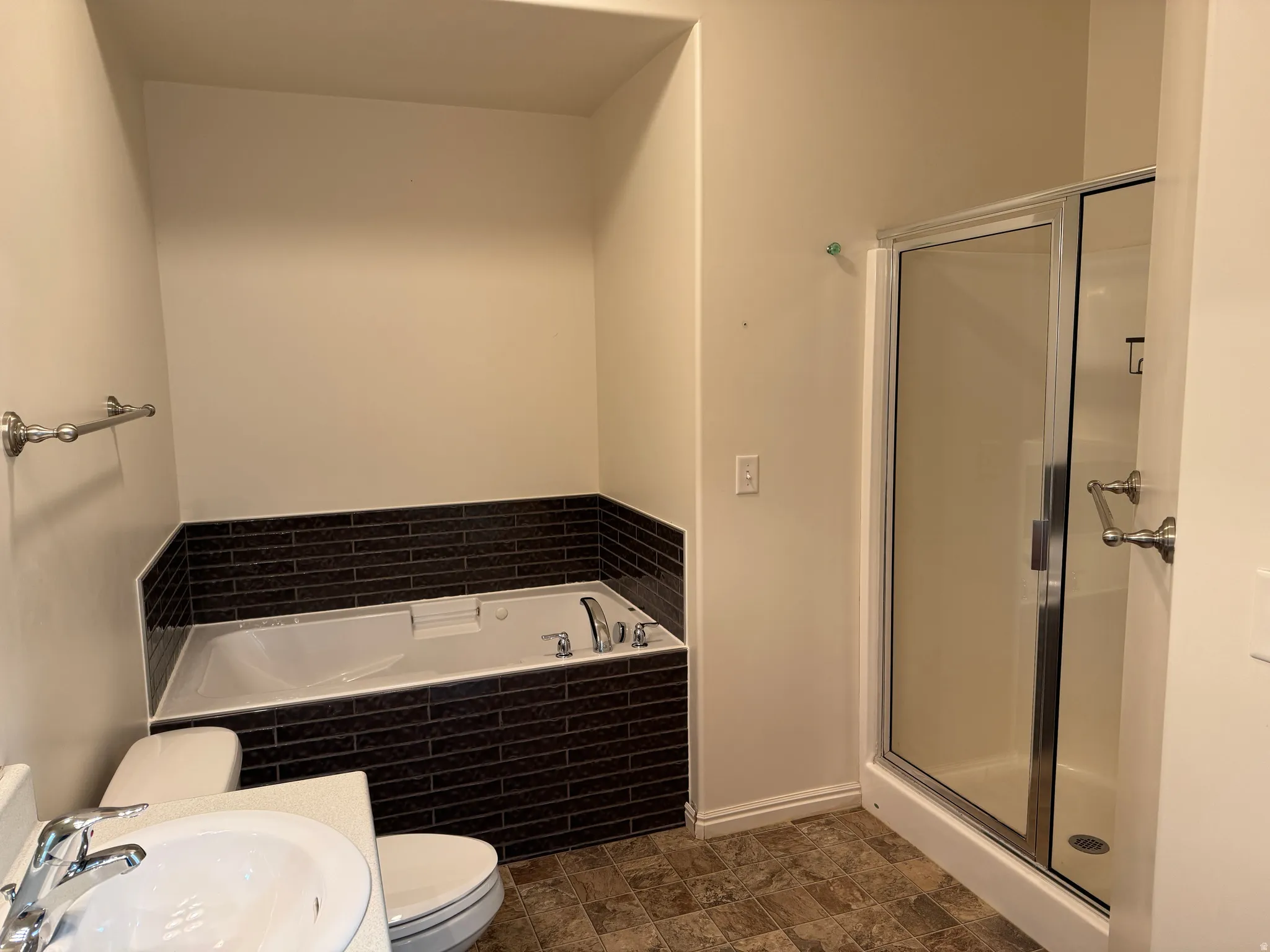 Bathroom featuring a jetted tub with dark tile surround, a separate glass-enclosed shower, and a vanity with an integrated sink