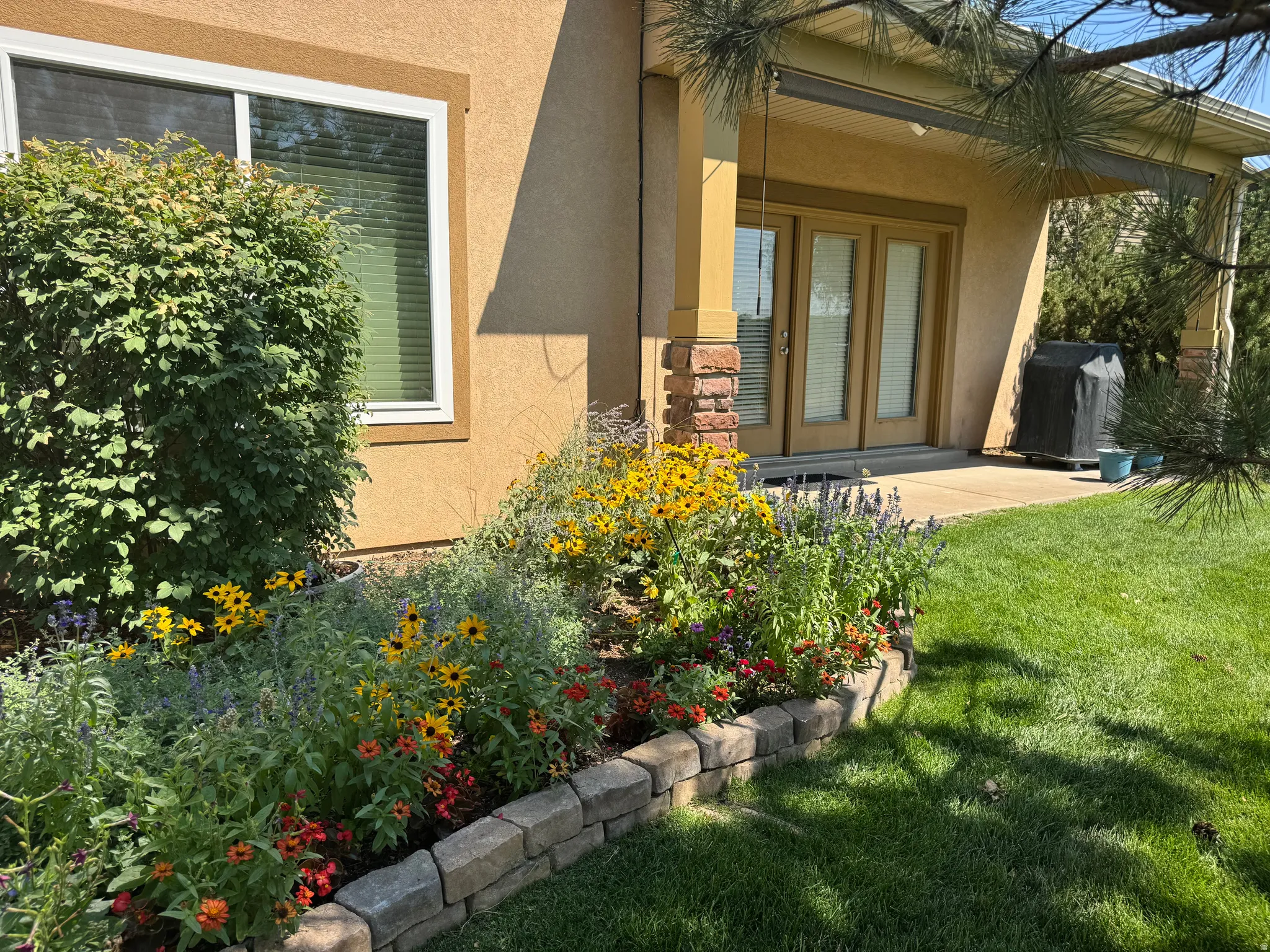 Landscaped backyard featuring a stone-edged flower bed, mature shrubbery, and a covered patio with French doors