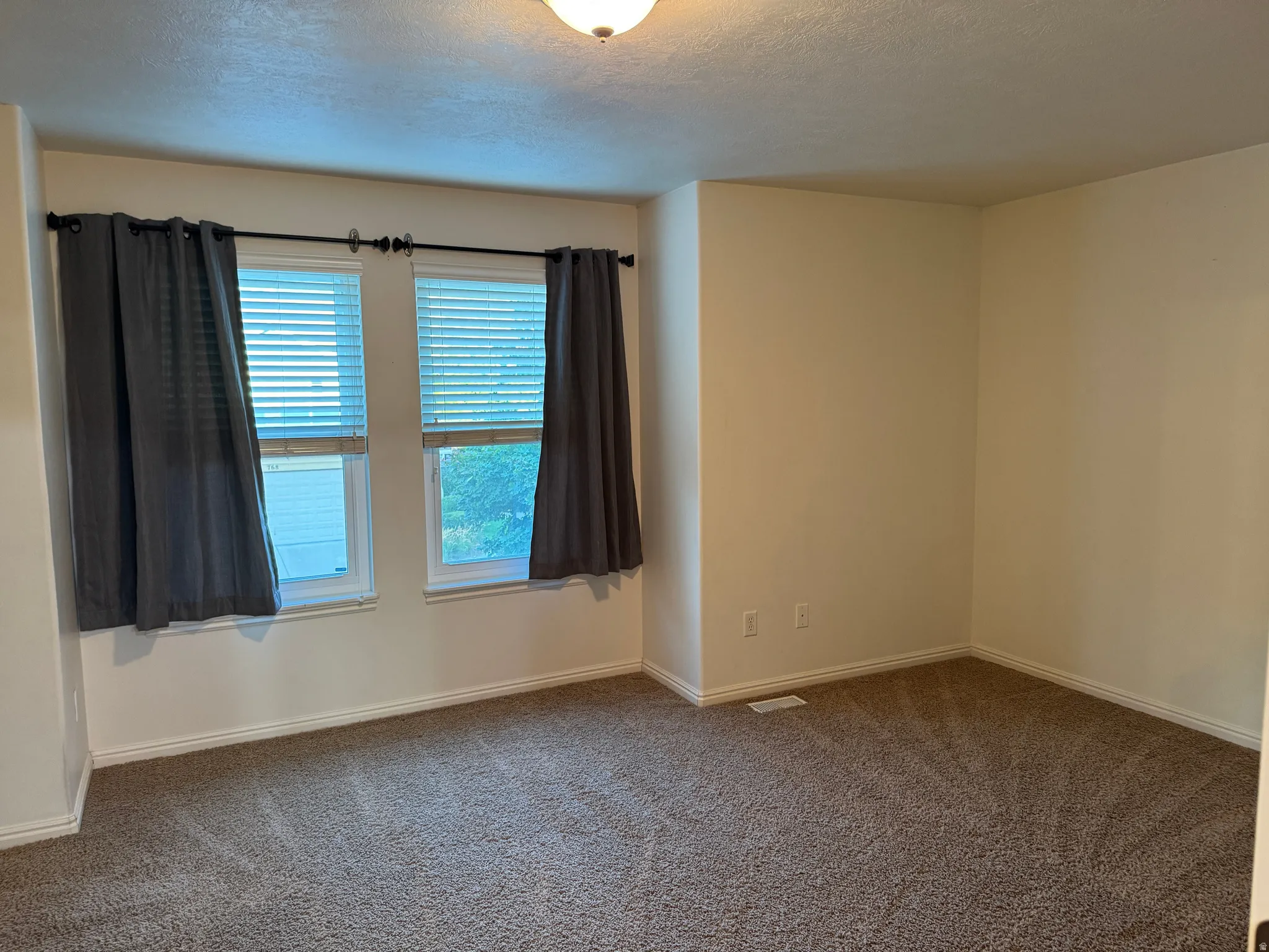 Carpeted room featuring two white-framed windows with blinds, neutral walls, and white baseboards