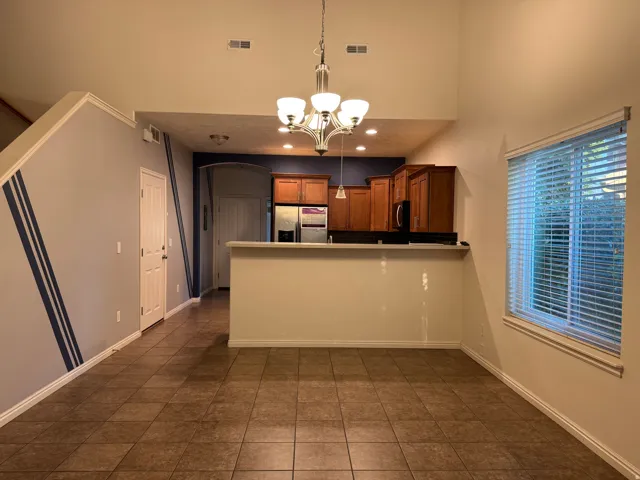 Open dining and kitchen area featuring a wood-finish island with breakfast bar seating, wood cabinetry with stainless steel appliances, tile flooring throughout, recessed lighting, and a pendant light fixture