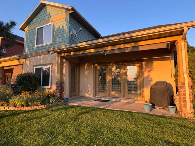 Charming two-story residence featuring a covered patio with wooden beam construction, expansive manicured lawn, and mixed siding exterior with upper-level gable detailing