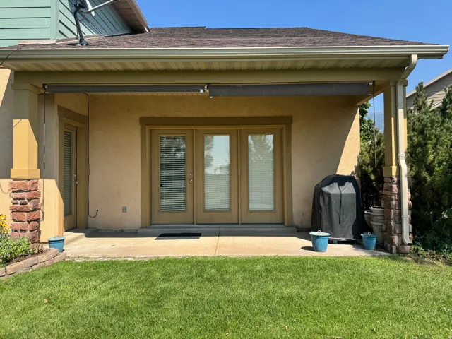 Ground-level patio with stucco exterior and French doors, featuring a retractable awning and brick-clad columns
