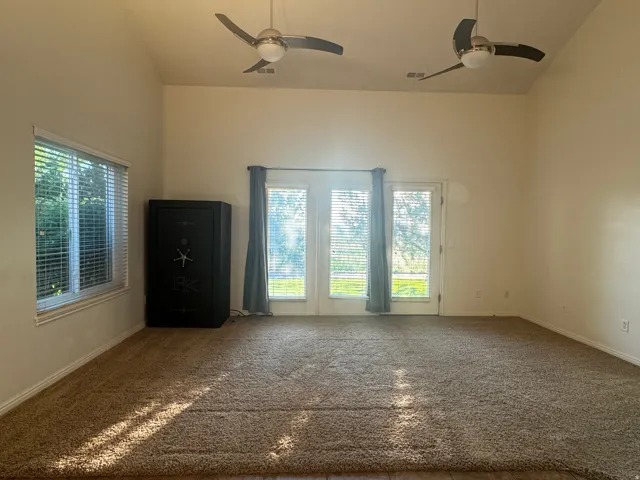 Spacious open room with dual ceiling fans, abundant natural light from triple glass doors and side window with plantation shutters, and neutral carpet flooring throughout