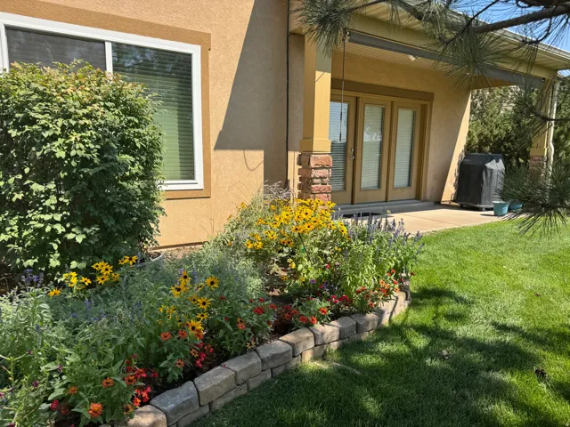 Landscaped backyard featuring a stone-edged flower bed, mature shrubbery, and a covered patio with French doors