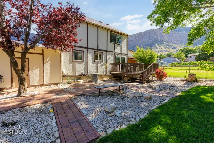 Expansive backyard featuring a multi-level wood deck, a brick paver pathway, gravel landscaping, manicured lawn, and mature trees