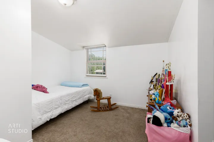 Bright and versatile bedroom featuring carpeted flooring, a single window with blinds providing natural light, and clean white walls