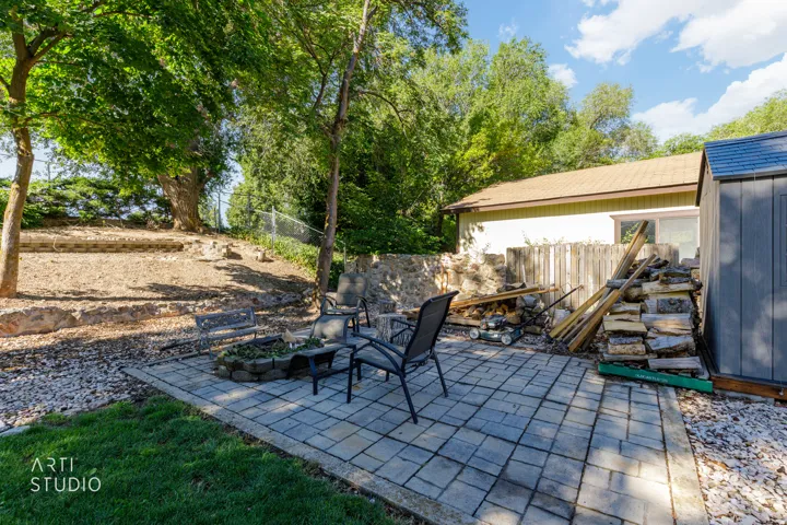 Stone paver patio featuring a built-in stone fire pit, surrounded by mature trees and a manicured lawn