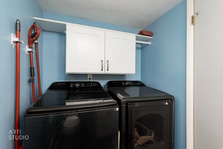 Dedicated laundry space featuring a built-in shelf, white upper cabinetry with dark hardware, and a clothes hanging rod