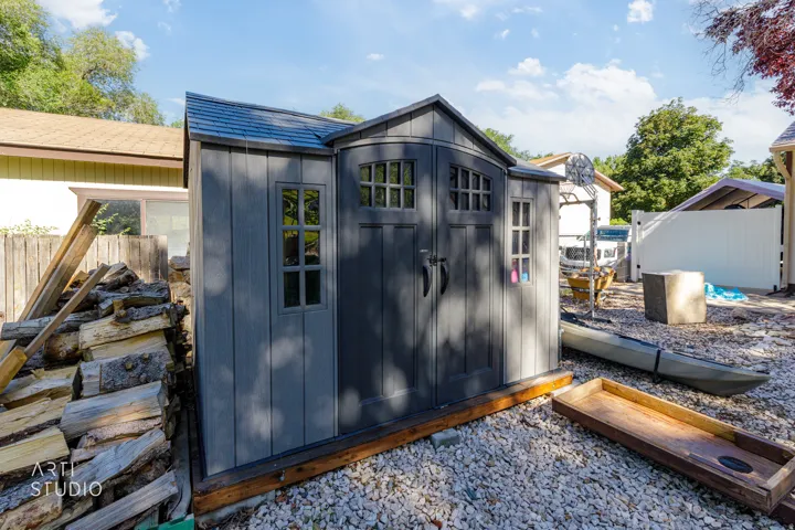 Spacious backyard shed featuring paneled doors, multiple windows, and a shingled roof